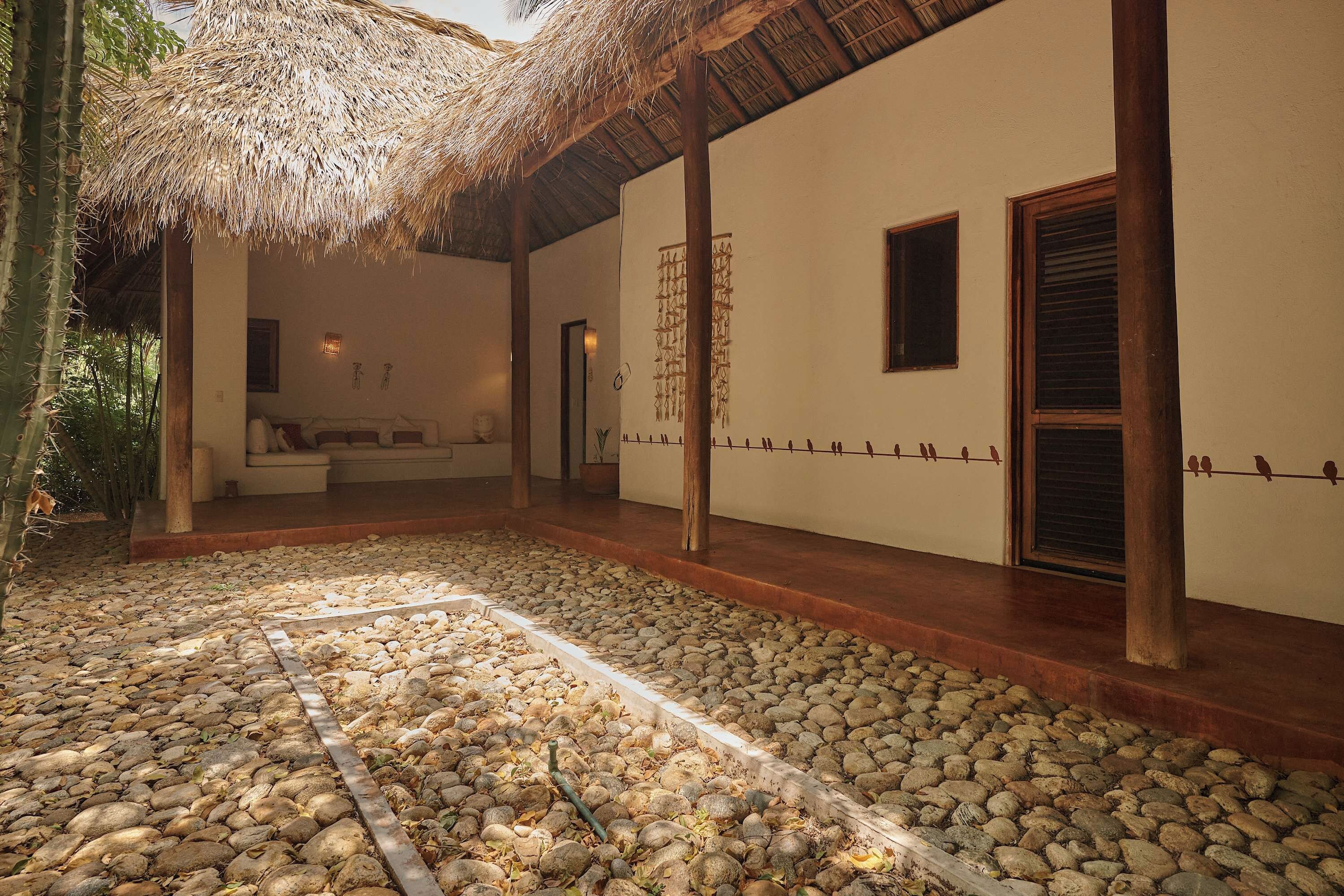 A covered outdoor area with a stone floor, a thatched roof, and a wall with a decorative line of birds.