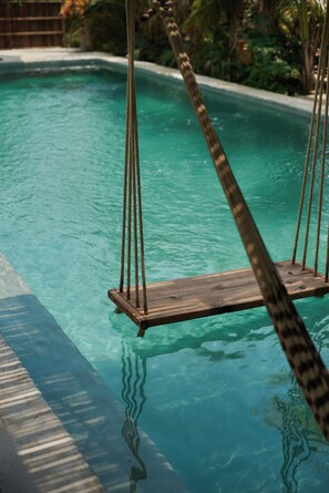 A clear swimming pool with a wooden swing chair in the center.