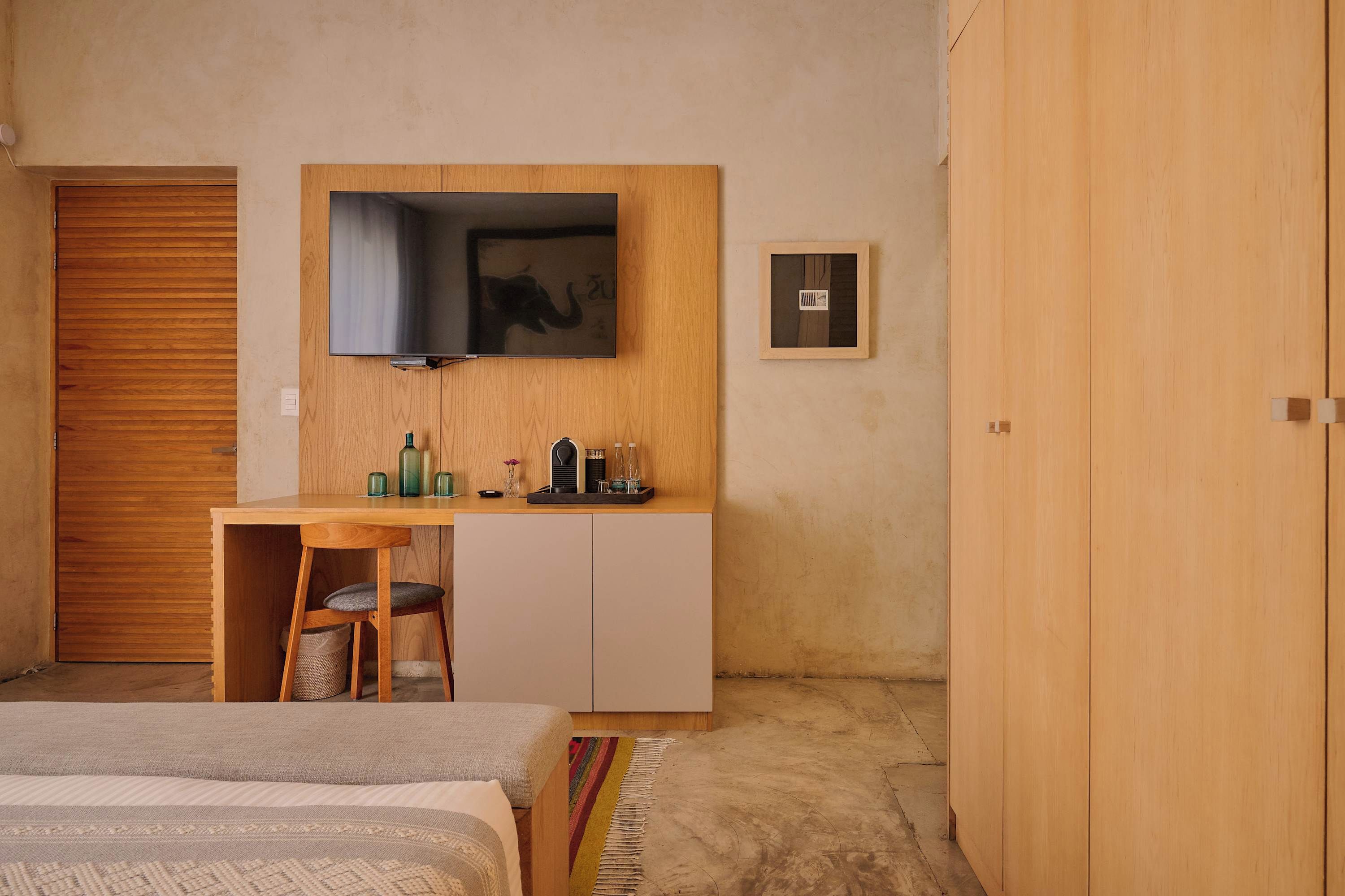 A bedroom with a bed, a desk with a chair, a wardrobe, and a television mounted on the wall.