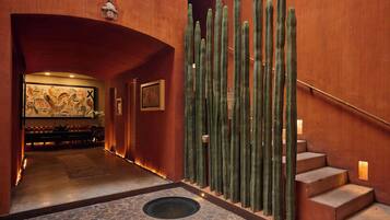 Een hotel lobby met een stenen vloer, een wand met cactussen en een trap.
