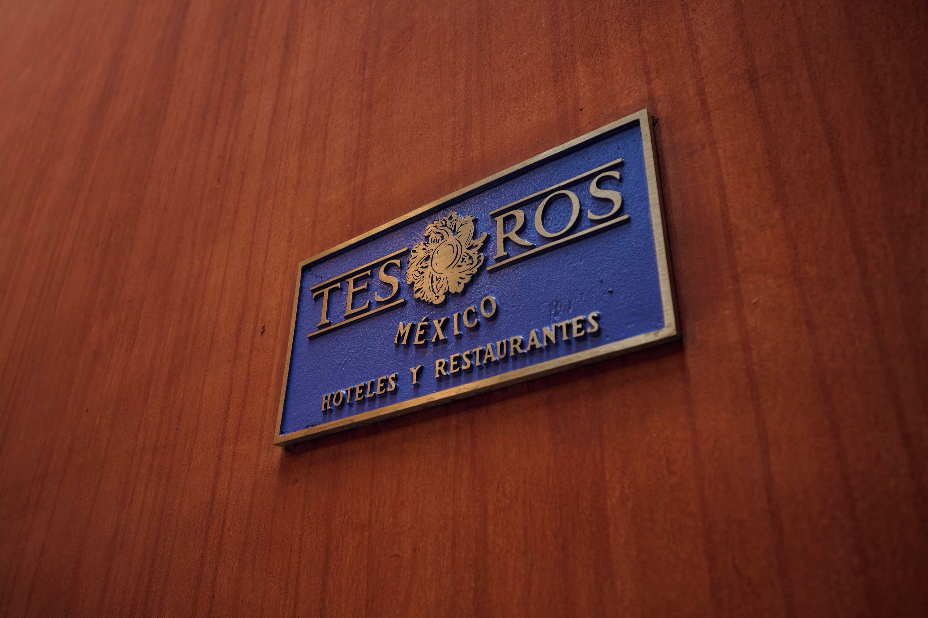 Een bord met de tekst 'TESOS MEXICO HOTELES Y RESTAURANTES' op een houten achtergrond.