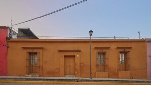 Un edificio con fachada plana, tres puertas y ventanas con barrotes.
