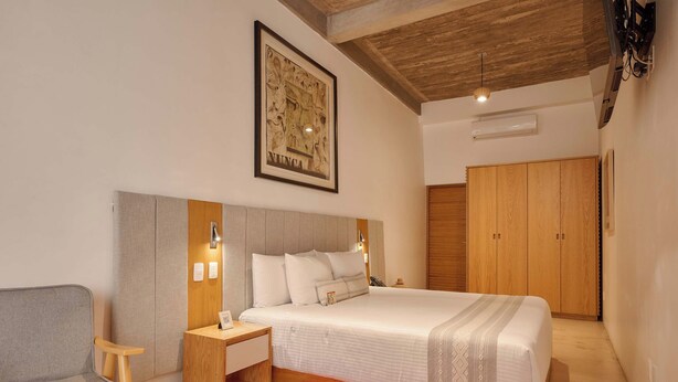 Un dormitorio con una cama grande, una mesita de noche, una silla, un armario y un cuadro en la pared.