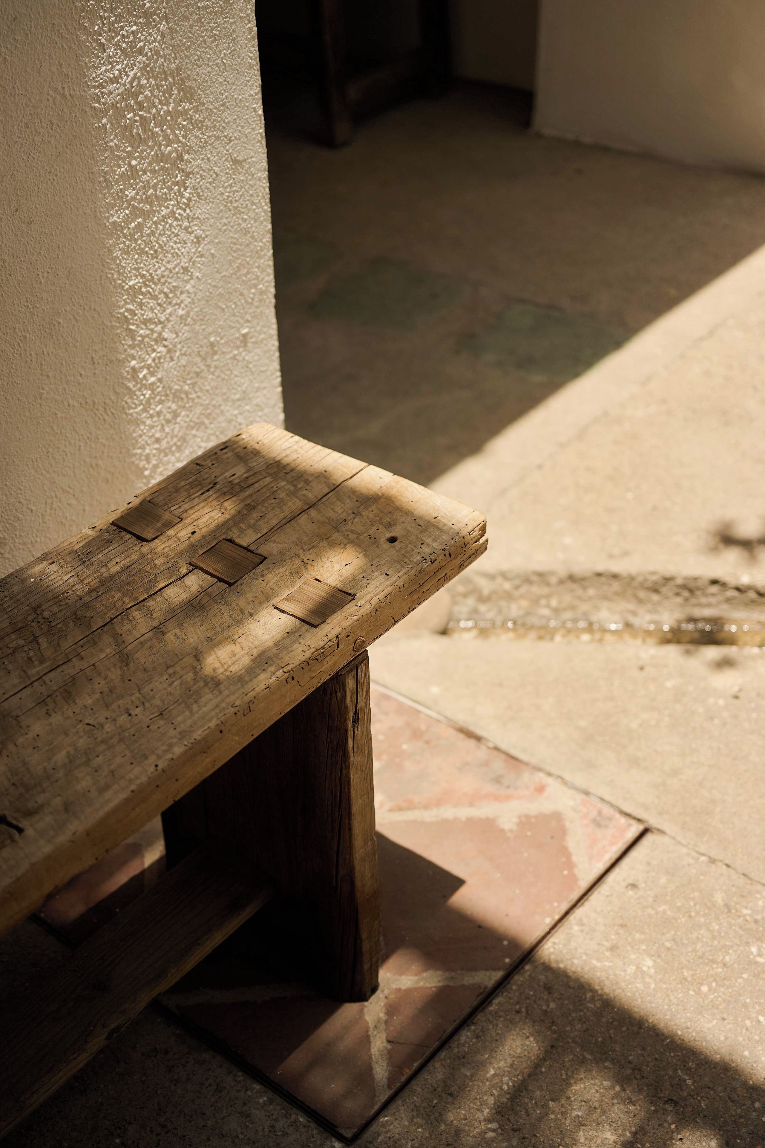A wooden bench with a slatted seat and backrest, positioned against a wall with a tiled floor.