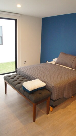 A bedroom with a bed, bench, and a view through a large window.