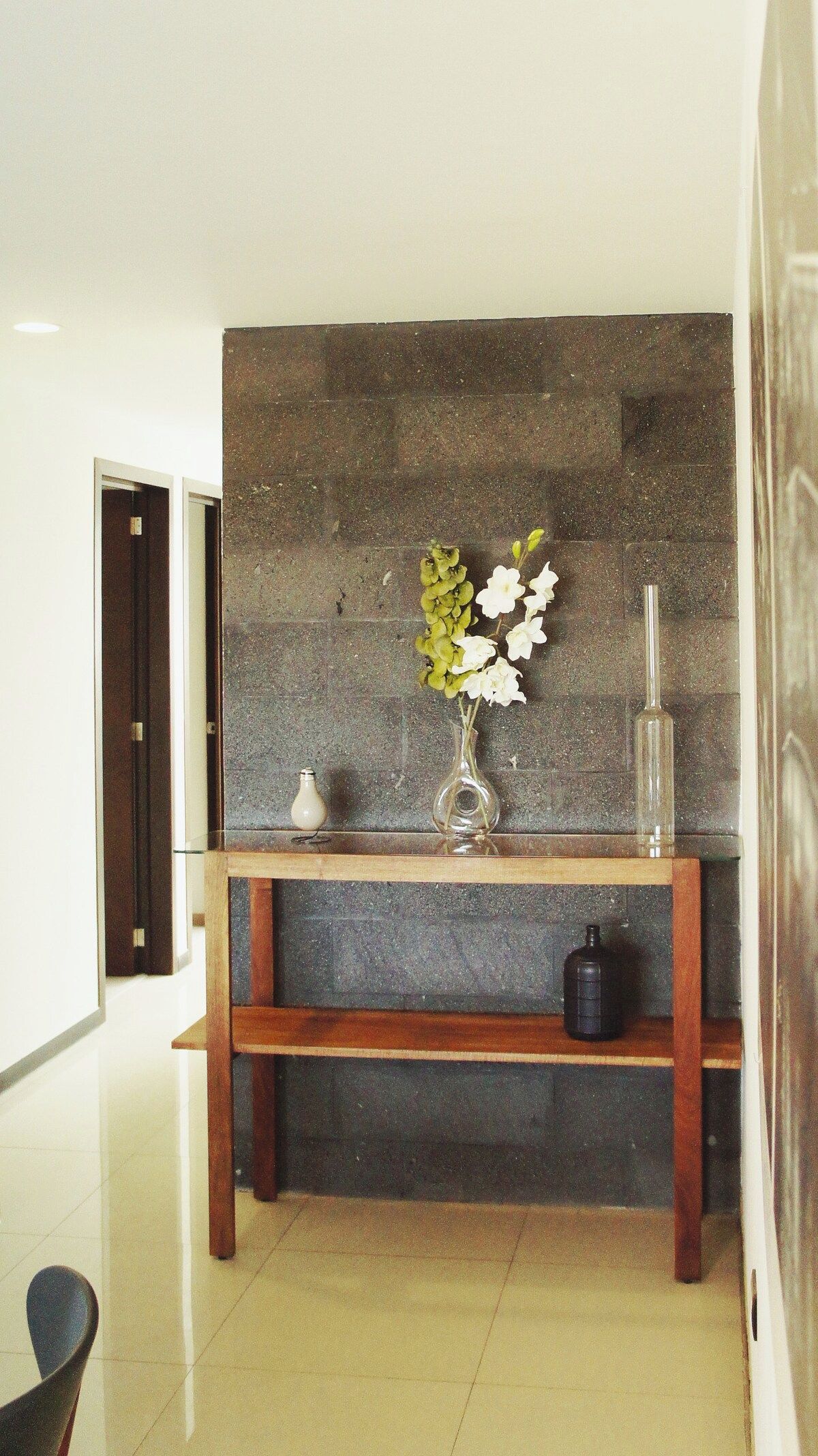 Un couloir avec une console en bois, un vase de fleurs et une bouteille.