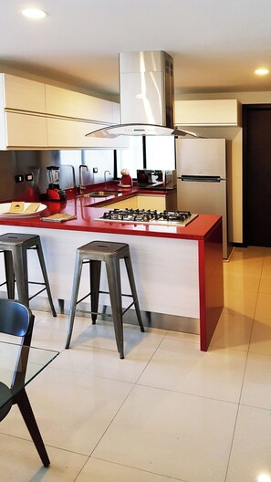 A modern kitchen with a central island, bar stools, a gas stove, and a stainless steel refrigerator.