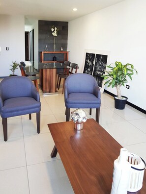 A modern living room with two blue armchairs, a wooden coffee table, and a potted plant.