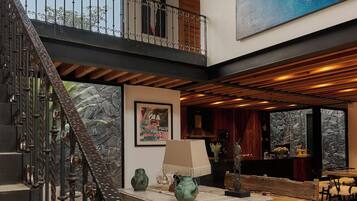 Un interior espacioso con techo alto, una escalera que lleva a un balcón y un mural grande en la pared.