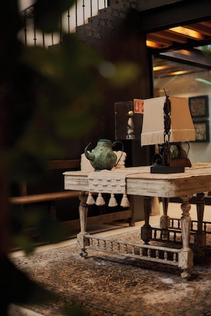 Een houten tafel in rustieke stijl, met een groene keramieken pot en een lamp met een witte kap.