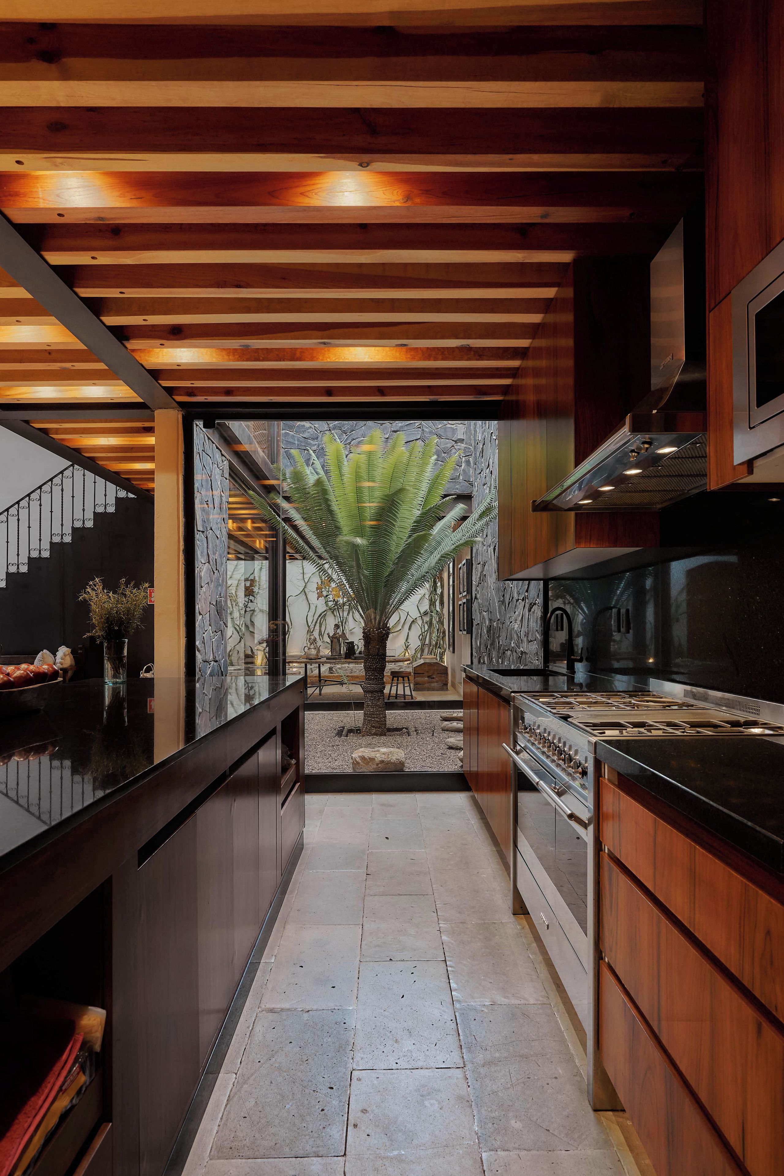 A modern kitchen with a central island, wooden ceiling beams, and a stone wall backdrop.