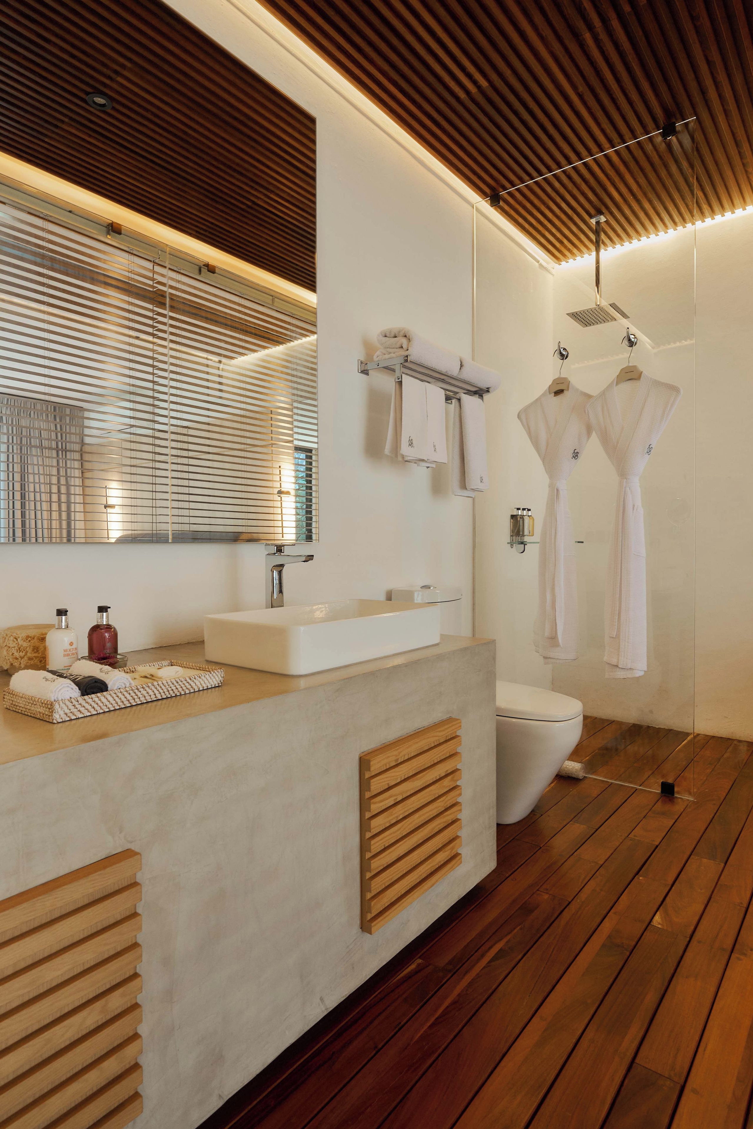 Een moderne badkamer met een houten vloer, een grote spiegel, een wastafel en een douche.