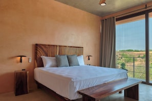 A bedroom with a large bed, bedside lamps, a wooden headboard, a bench, and a view through a large window. - 5-bedroom house steps from the beach (Puerto Escondido)
