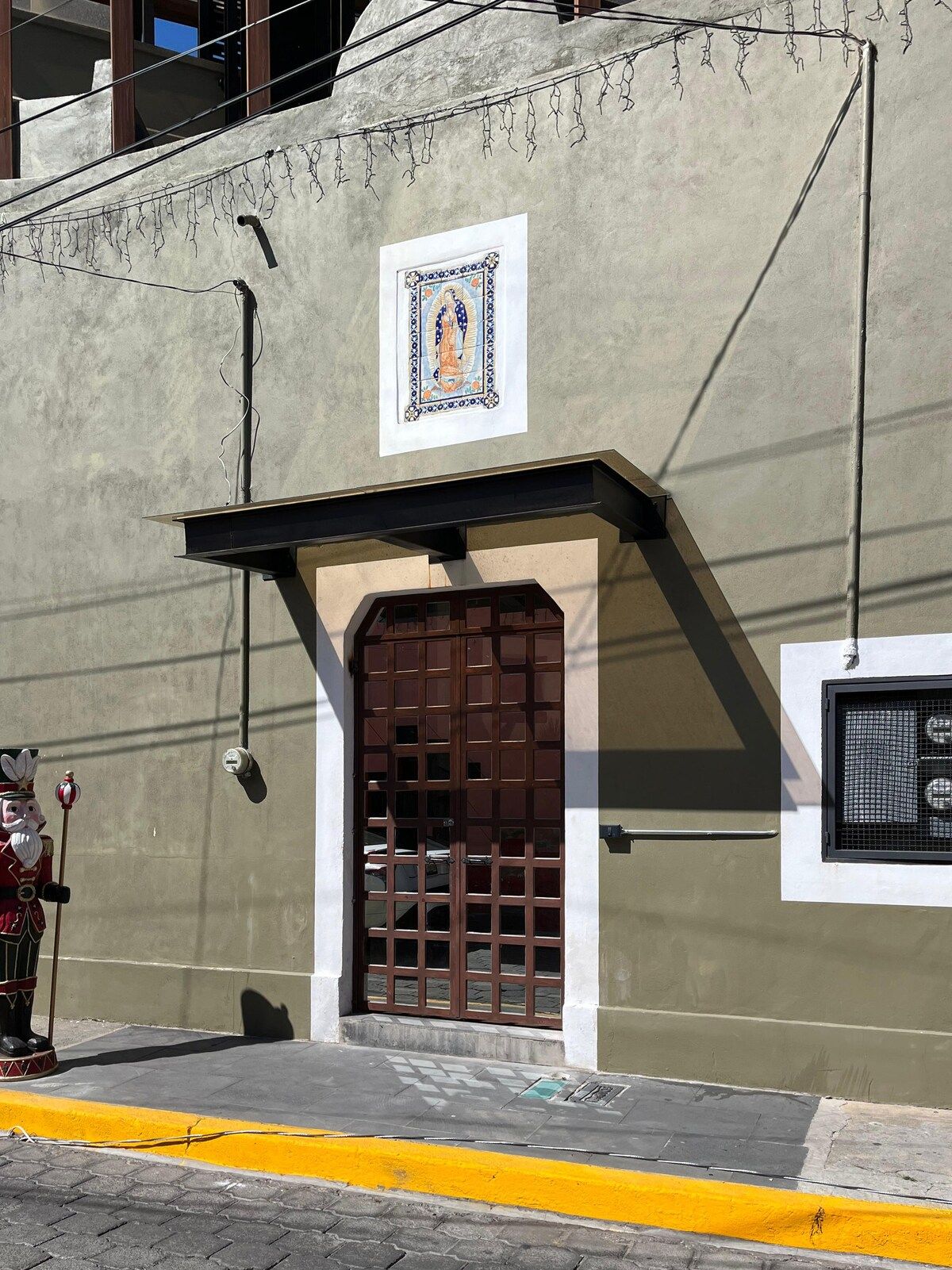 Fachada de edifício com azulejo decorativo, porta marrom e calçada amarela.