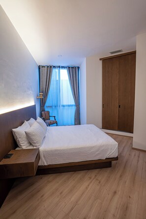 A modern bedroom with a large bed, a wooden nightstand, a chair, and a wardrobe. - Laurelian 8 · Eles · 2 BR Apt near downtown (Oaxaca de Juárez)
