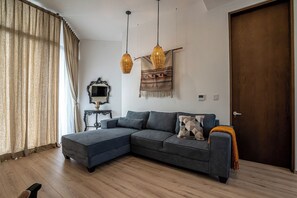 A modern living room with a sectional sofa, pendant lights, a decorative tapestry, and a wooden door. - Laurelian 8 · Eles · 2 BR Apt near downtown (Oaxaca de Juárez)