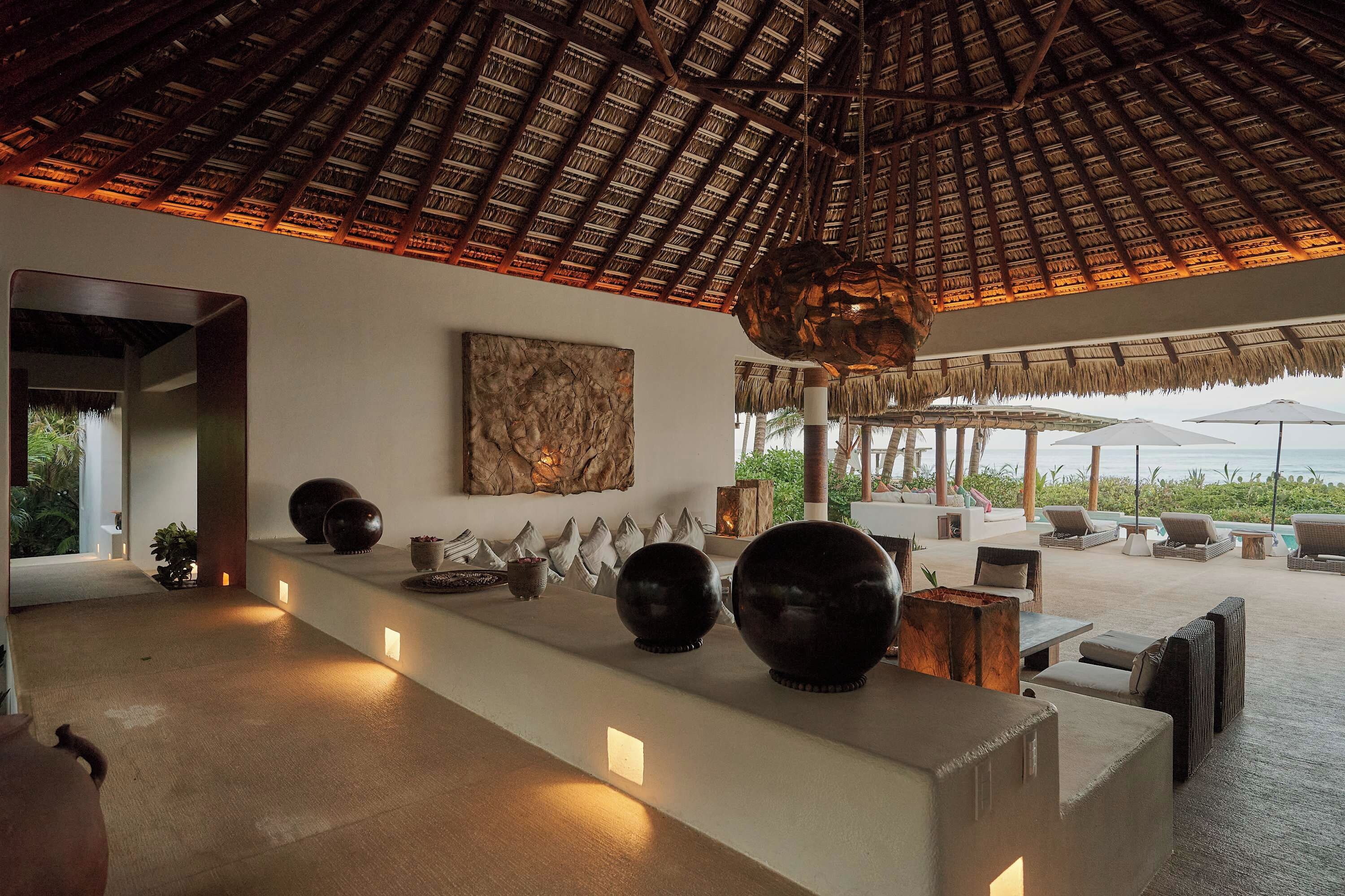 Un interior moderno con techo de paja, una recepción con cuencos decorativos y vistas al exterior.