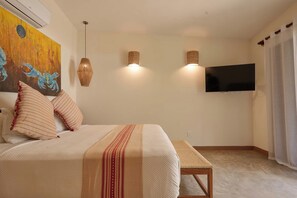 A bedroom with a bed, a painting, two wall-mounted lights, a television, and a window with curtains. - Casa Juliana · Private suite · Beachfront property (Puerto Escondido)