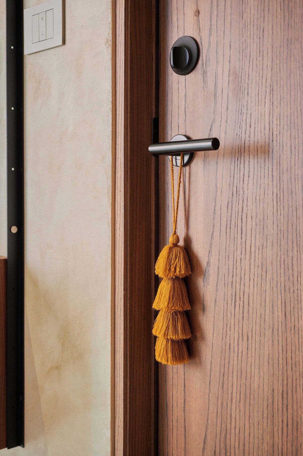 A wooden door with a black handle, a keyhole, and a yellow tassel hanging from a hook.