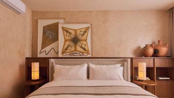 Une chambre d’hôtel avec un lit, deux lampes fixées au mur et une étagère où sont posées des objets en céramique.