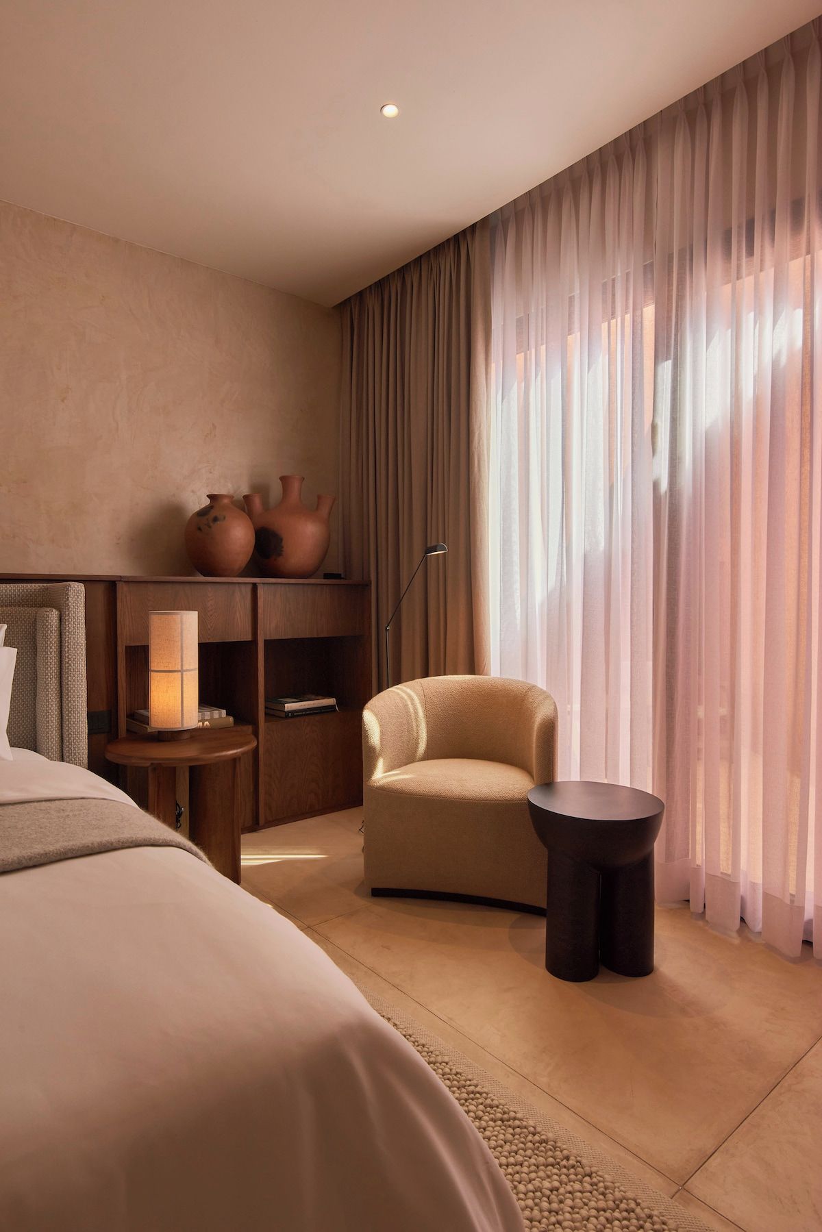 Ein Hotelzimmer mit einem Bett, einem Sessel, einem kleinen Tisch, einer Lampe und einem Regal mit Dekoration.