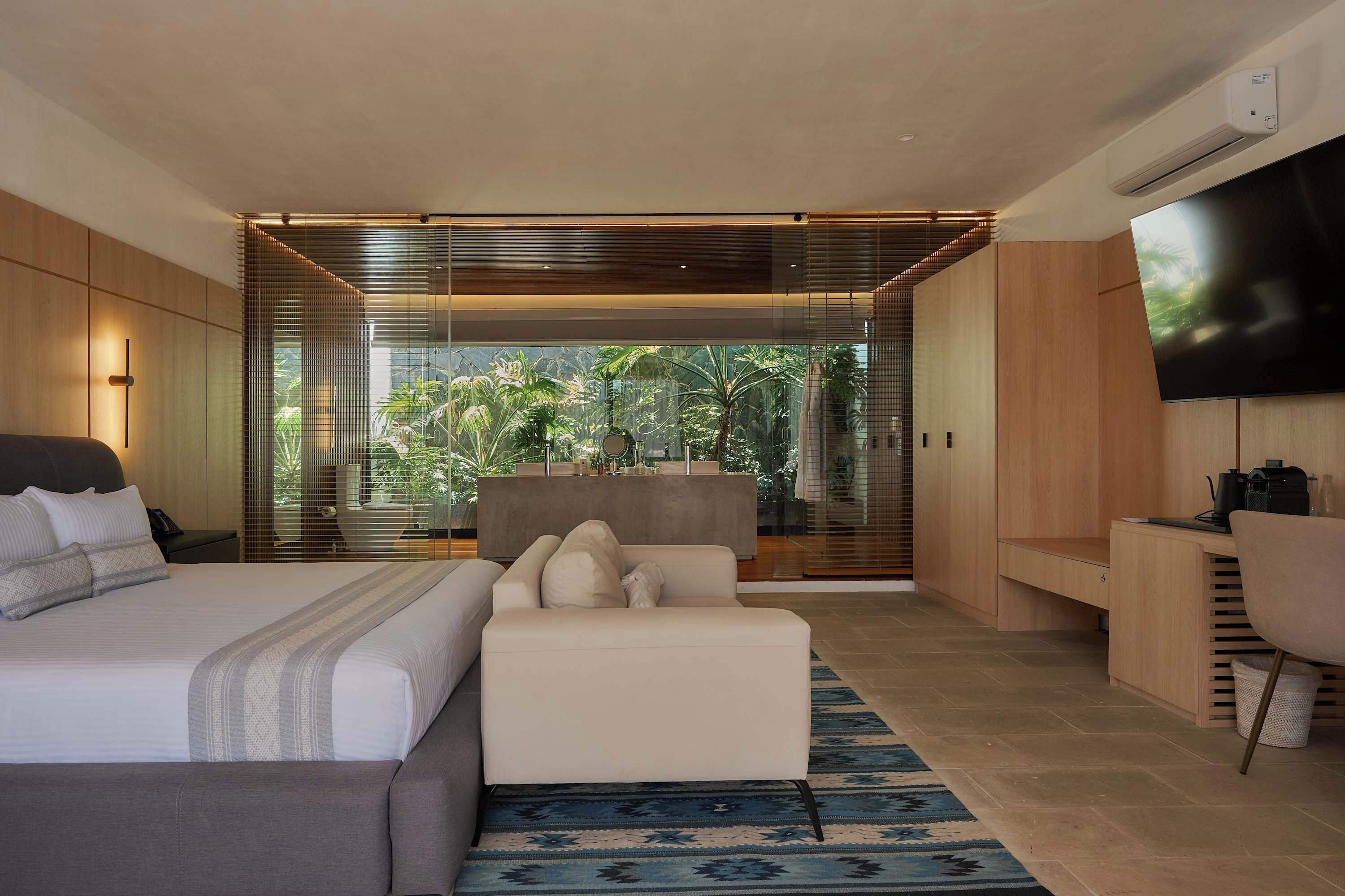 Une chambre moderne avec un grand lit, un canapé, une télévision et une vue sur la verdure.