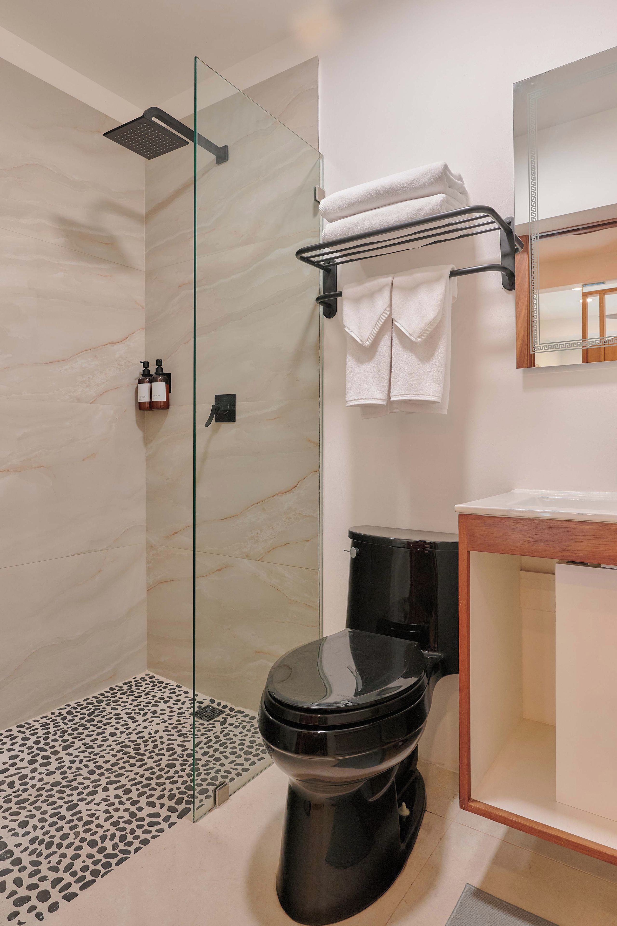 A modern bathroom with a glass-enclosed shower, a black toilet, and a wooden vanity.