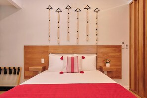Ein Schlafzimmer mit hölzernem Kopfteil, einem Bett mit weißer und roter Bettwäsche sowie einer Wanddekoration mit einem Quastenbesatz.