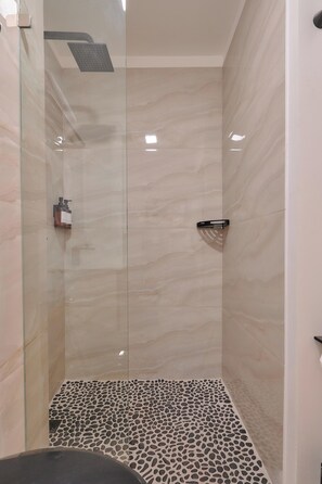 Eine moderne Dusche mit Glastür, Duschbrausehandstück und Boden in Kieselsteinmuster.