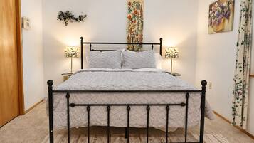 A bedroom with a four-poster bed, two bedside lamps, a floral tapestry, and a painting on the wall.