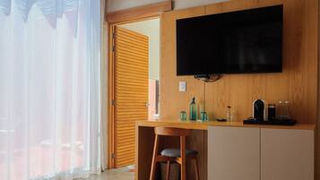 Una habitación de hotel moderna con una cama, un escritorio, un televisor y vistas al exterior a través de una ventana con cortinas translúcidas.
