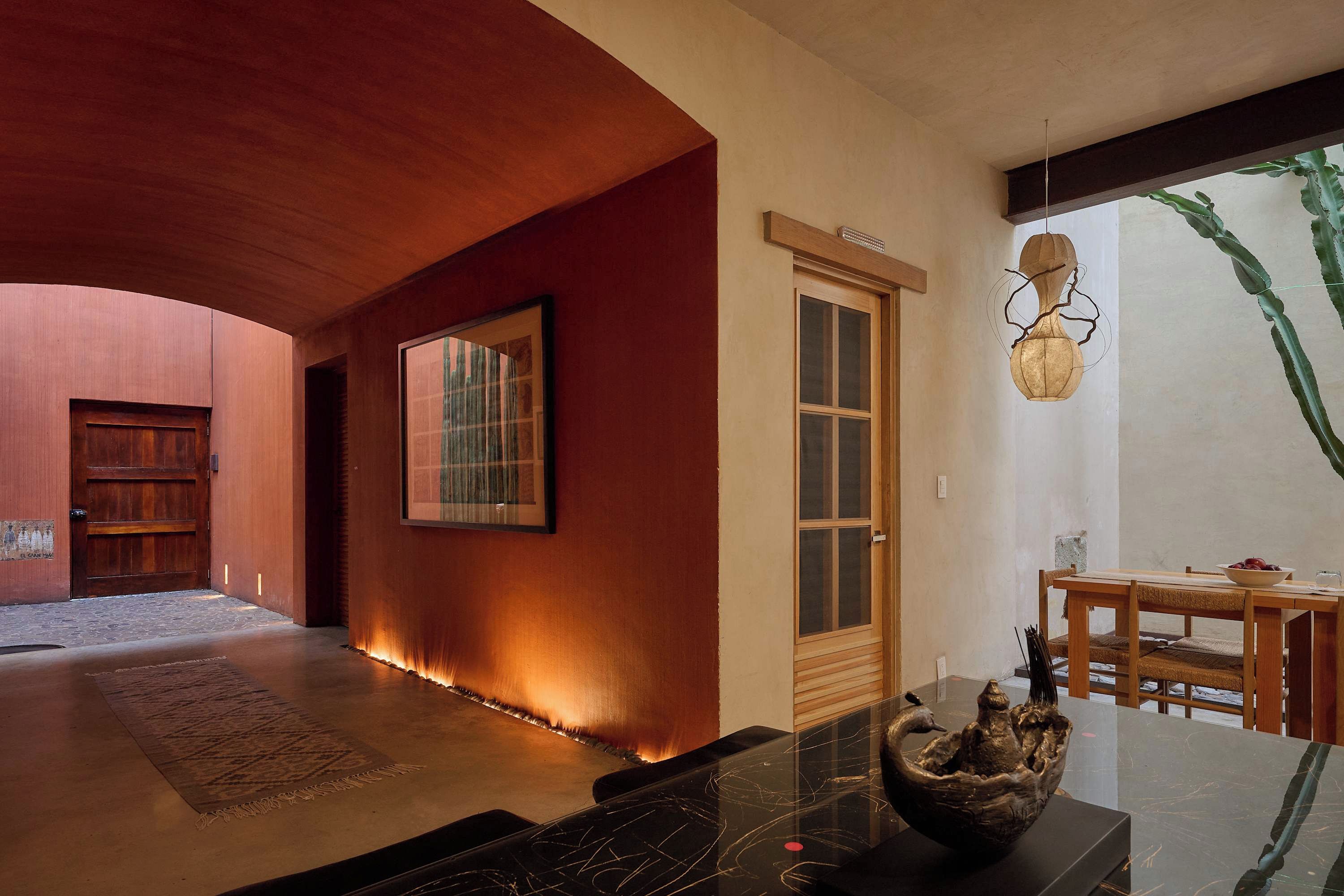 Un interior moderno con techo curvo, puerta de madera, un cuadro enmarcado y un comedor con mesa y sillas.