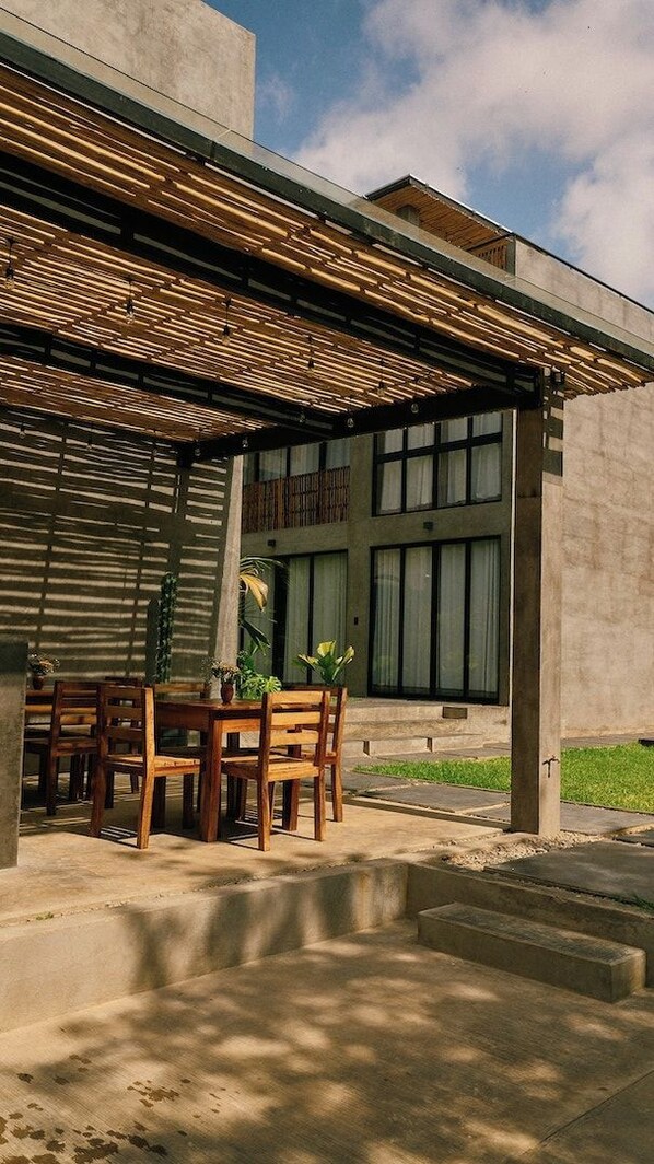 An outdoor seating area with a table and chairs, a pergola, and a building with large windows.