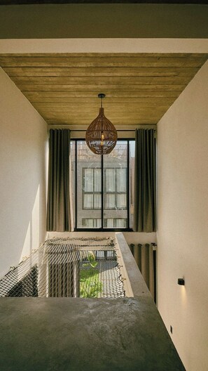 Quarto com um banco de concreto, luminária pendente e janela com cortinas.