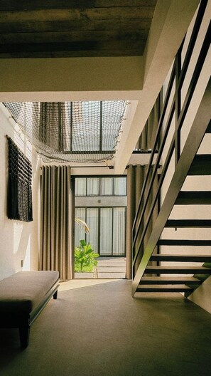A modern interior with a staircase, a bench, and a view of greenery outside.