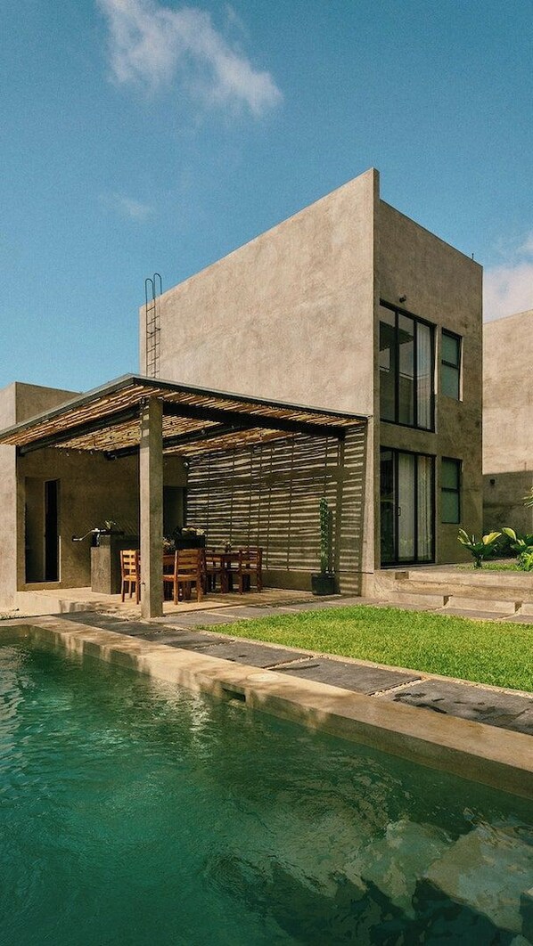 Uma casa moderna com piscina, varanda coberta e gramado bem cuidado.