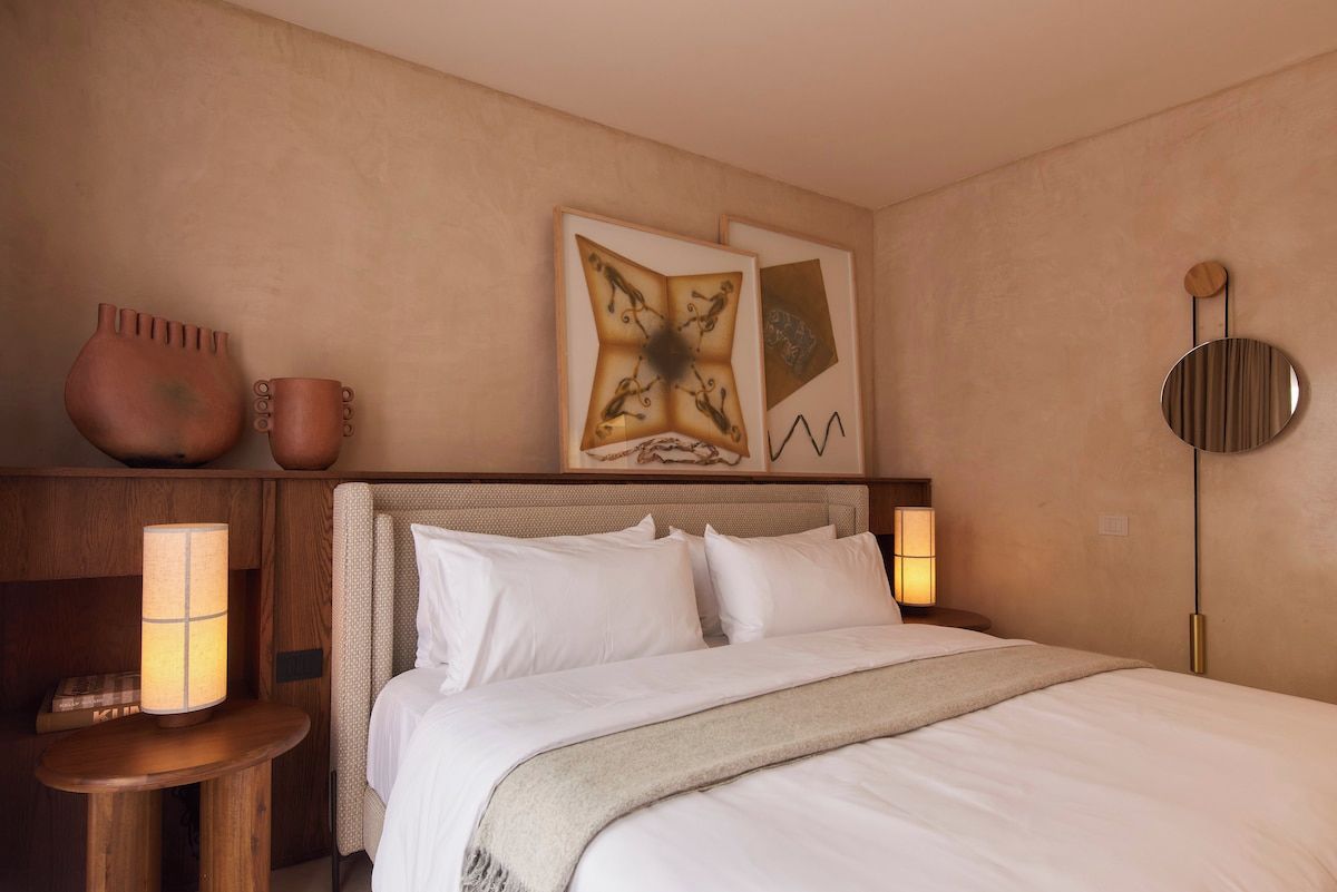 A hotel room with a bed, bedside lamps, a nightstand, and wall art.