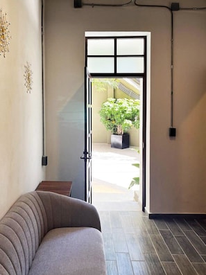 An interior space with a sofa, a door leading to an outdoor area with a potted plant, and a wall-mounted light fixture.