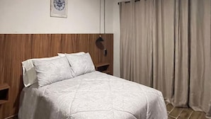 Hotellihuone, jossa on sänky, yöpöytä, seinään kiinnitetty lamppu ja ikkuna, jossa on verhot.