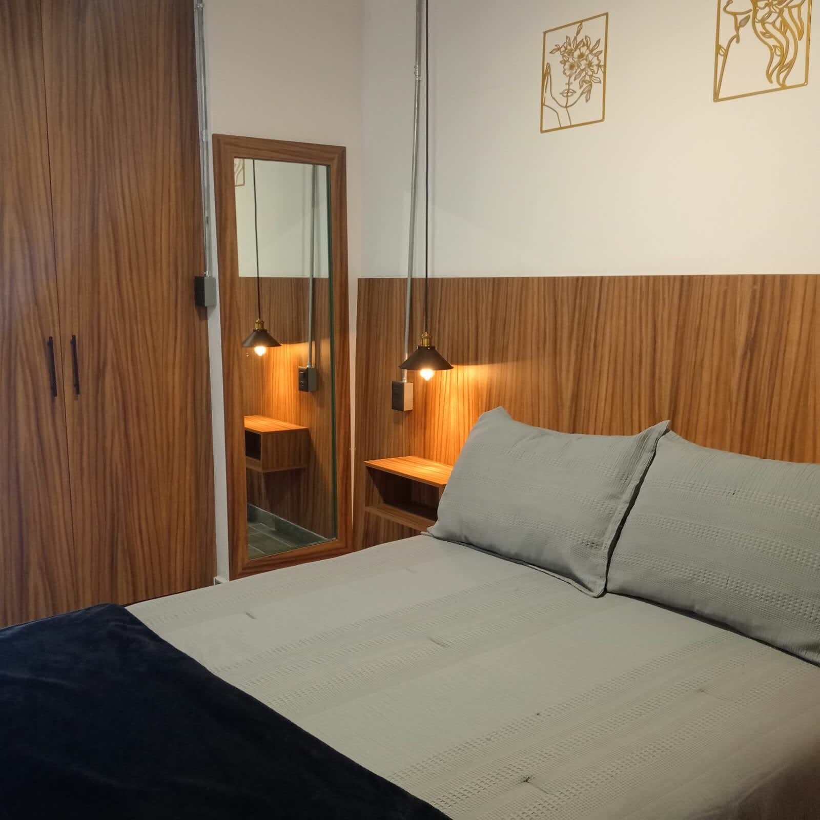 Une chambre avec une armoire en bois, un lit avec un oreiller gris et deux lampes suspendues.