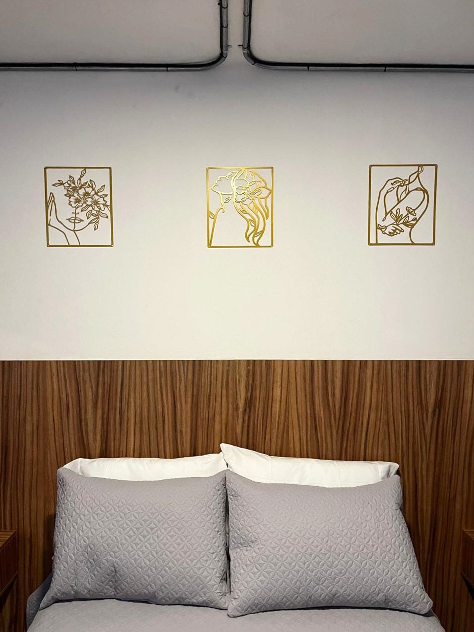 A bed with grey bedding, a wooden headboard, and three framed artworks on the wall above.