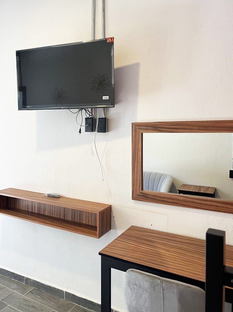 Quarto moderno com televisão de tela plana na parede, mesa de consola de madeira, espelho e uma cadeira.