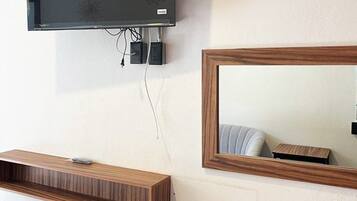 Quarto moderno com televisão de tela plana na parede, mesa de consola de madeira, espelho e uma cadeira.