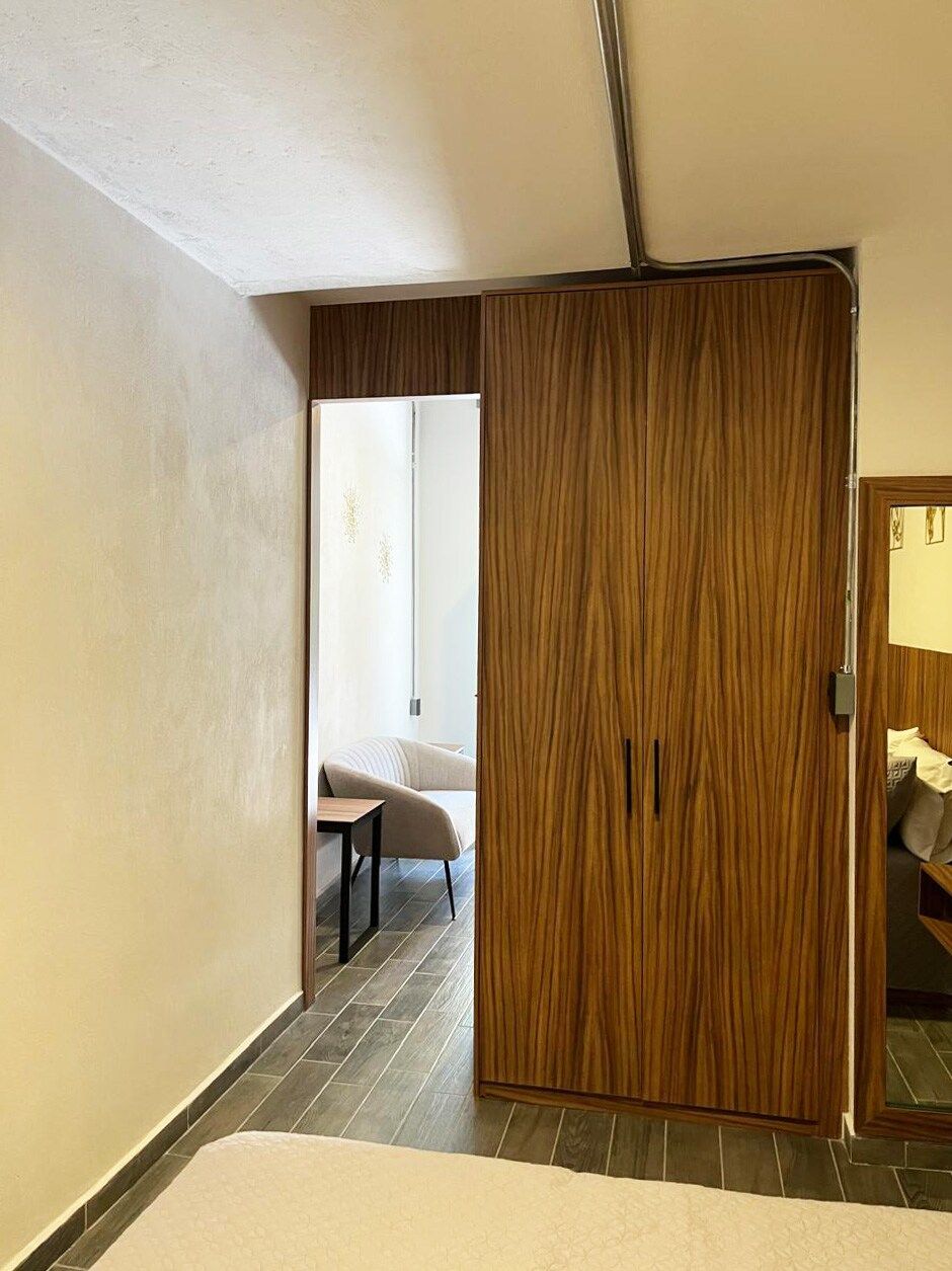 A room with a wooden wardrobe, a small table, and a chair.