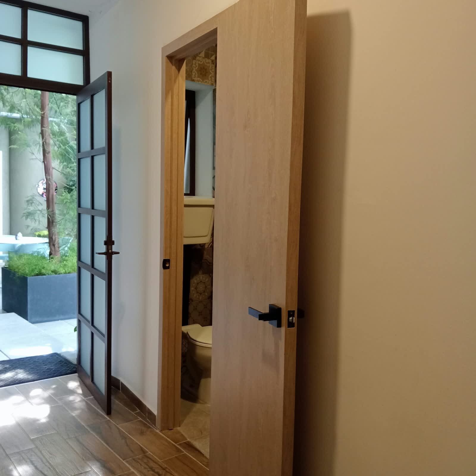 A wooden door leading to a bathroom with a toilet and a shower area.