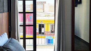 Hotellihuone, jossa on sänky, ikkuna verhoilla, näkymä ulos ja peili seinällä.
