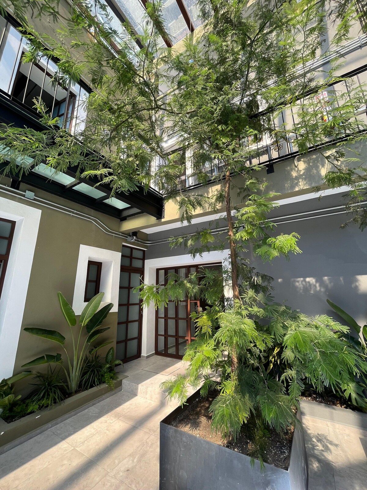 A modern building with large windows, a courtyard with plants, and a metal staircase.