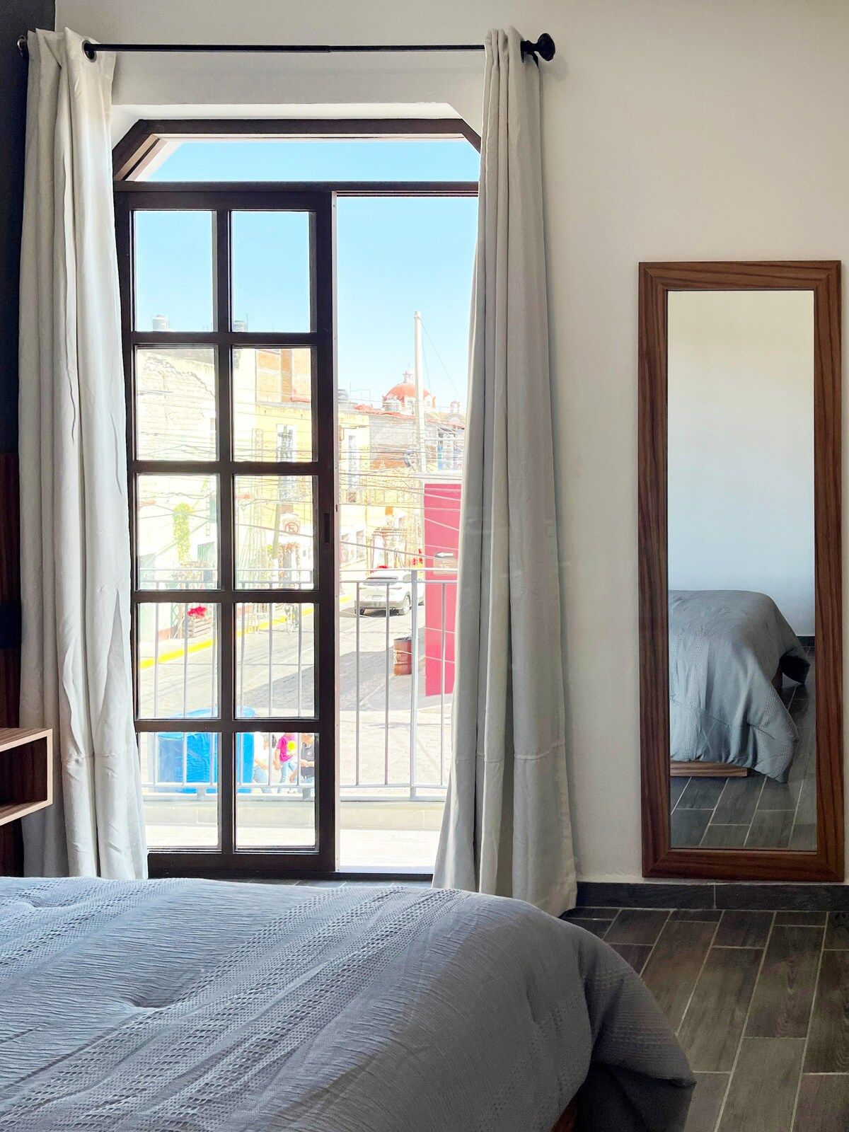 Une chambre avec une grande fenêtre, un lit et un miroir.