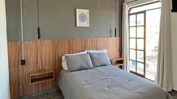 Ein modernes Schlafzimmer mit einem Bett, einem Holz-Kopfteil, einer Wandleuchte und einem Fenster mit Vorhängen.