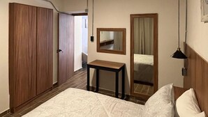 Hotellihuone, jossa on sänky, pieni pöytä, peili ja vaatekaappi.